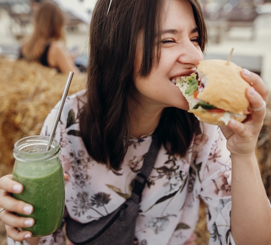 female eating vegan burger and smoothie cropped
